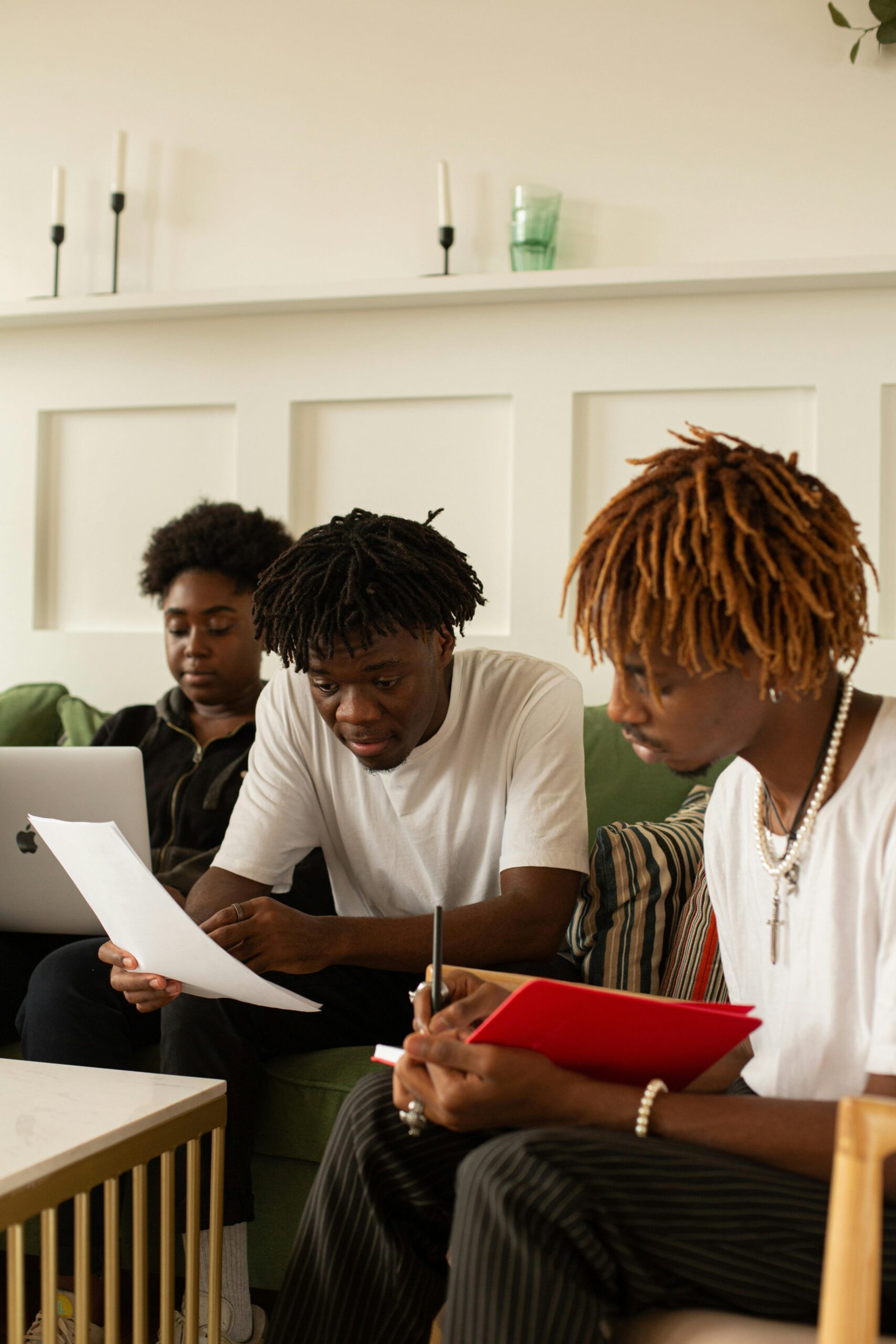 Three students engage in study session with laptops and notebooks indoors.